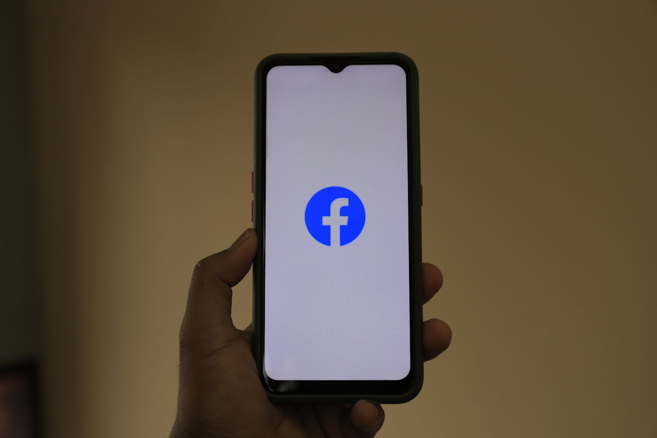 mobile-01 A smartphone held in hand showing the Facebook logo on its screen.