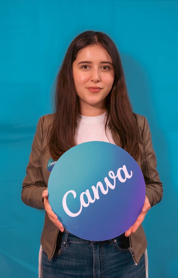 creative-01 Portrait of a young woman holding a Canva logo sign, with a blue background.